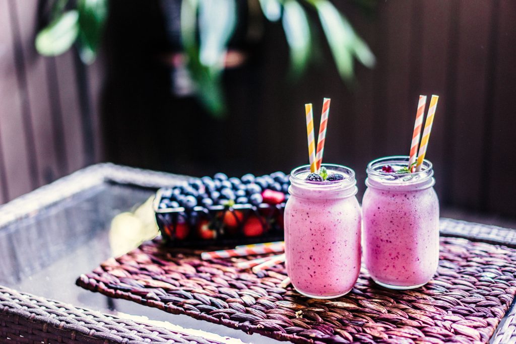 blueberry and cranberry smoothies on a table with fresh berries and straws