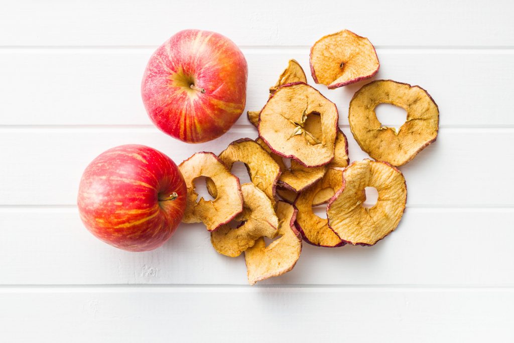 dried apple slices and whole red apples on a white table