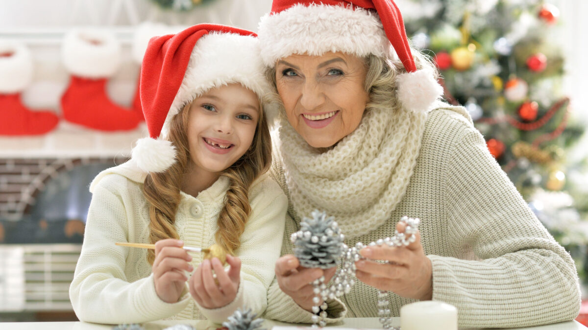 a senior woman and her granddaughter, wearing Santa hats and crafting