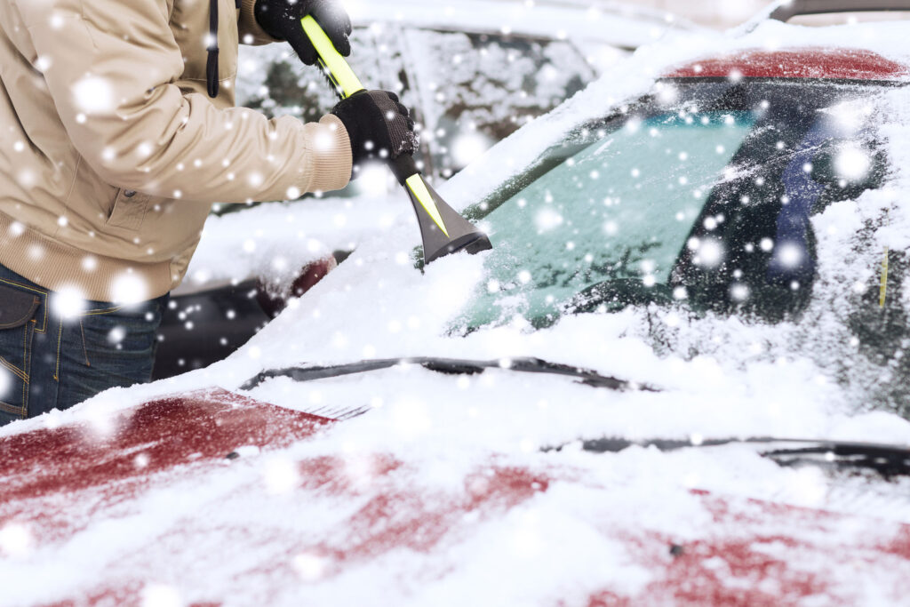 a senior man brushing snow from his car’s windshield