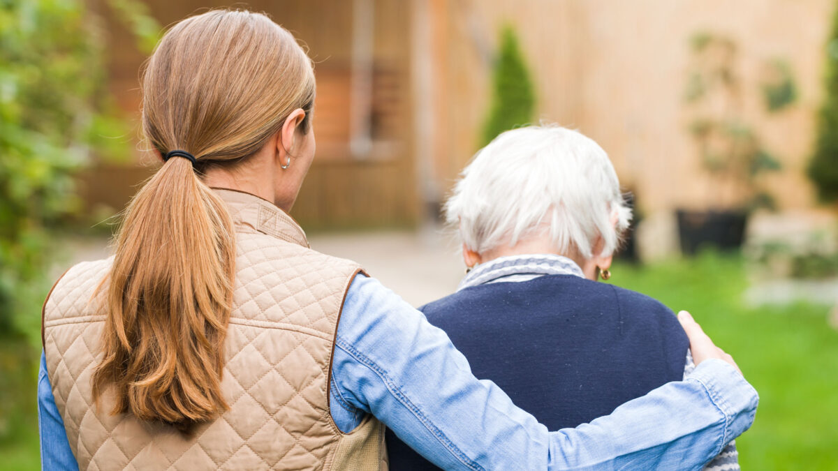 a younger woman walking outside with her arm around an older woman’s shoulders